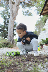 Little boy crouching in a garden, concentrating on maneuvering a remote-controlled toy car....