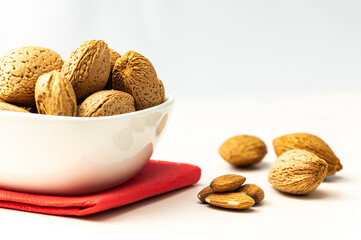 Almonds in white bowl, next to shelled almonds, on white wooden surface.