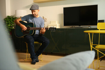 A man sitting at home learning to play a chord on acoustic guitar