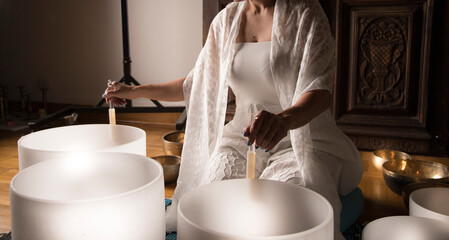 Woman practicing so und healing with crystal bowls, creating soothing vibrations for meditation,...