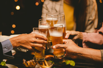 A cheerful group of young adults enjoys a lively night out, raising glasses in a celebratory toast. Laughter and smiles fill the air as friends bond over drinks in a vibrant social gathering.