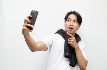 Fototapeta premium Excited Young Asian Man in Casual Outfit Holding Smartphone and Pointing with Joyful Expression