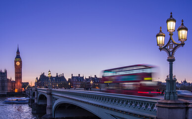 Red double-decker bus crosses Westminster Bridge at dusk with Big Ben in the background