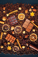Background of coffee beans, dark and milk chocolate pieces, cinnamon, dried orange and star anise.
