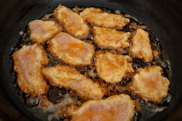 Chicken breast meat fillets with egg in boiling oil in a pan, flat lay close up