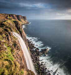Majestic waterfall cascading down cliffs into the ocean under a dramatic sky during sunset