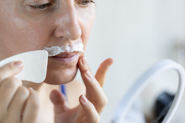 Woman in front of the mirror applying depilatory cream above the upper lip.