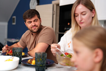 A man and a woman sit at a kitchen table eating lunch while a young child sits beside them