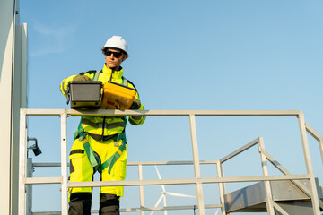 Front view of wind turbine worker or technician man stand on base of windmill and check tools in the toolsbox with day light.