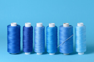 Row of blue thread spools with needle aligned background with copy space for text close-up flat lay top view