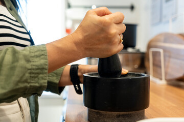 Female hand holds pestle, grinding spices in traditional mortar for cooking