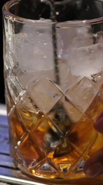 Close up of a professional bartender is mixing an alcoholic cocktail with professional crystal long lasting ice cubes to customers at the bar or disco club. Professional bartender masterly creating
