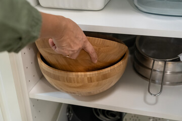 Female hand reaches for wooden bowls on kitchen shelf with various kitchenware