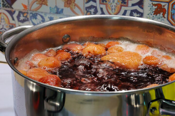 A Stainless Steel Pot Filled With Peaches Simmering In Red Liquid On A Stove. The Colorful Tiles In The Background Add To The Kitchen's Vibrant Atmosphere.