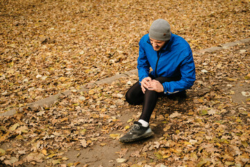 Knee pain. Sports injury. The young man felt pain in his knee during an outdoor workout. A sports knee injury while running at a runner in an autumn park.