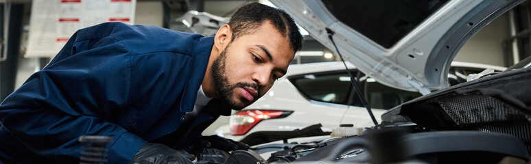 A focused young mechanic inspects the engine of a car in a lively auto repair workshop.