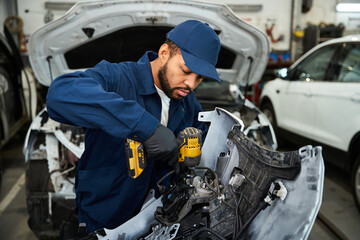 A handsome young mechanic focuses on fixing a vehicle in a busy automotive garage.