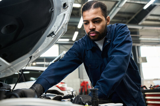 A skilled mechanic focuses intently while repairing an engine in a bright garage.