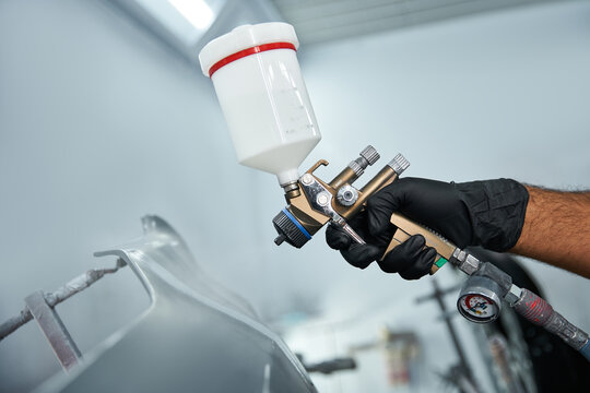 A skilled mechanic is applying paint to a car with precision in a well equipped garage.