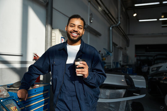 Confident young mechanic sips coffee, surrounded by tools and equipment.