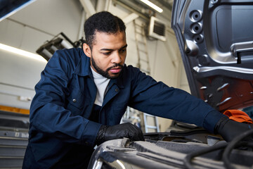 Dedicated young mechanic focuses on maintaining a car in a lively repair shop setting.