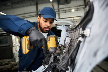 Handsome young mechanic focuses intently while repairing a vehicle in his workplace.