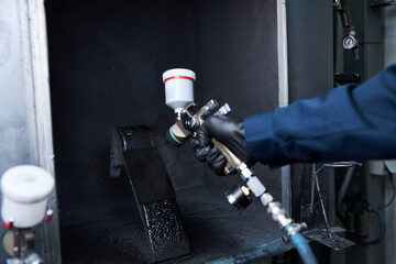 Handsome young mechanic focuses on painting a car part in a professional workshop setting.