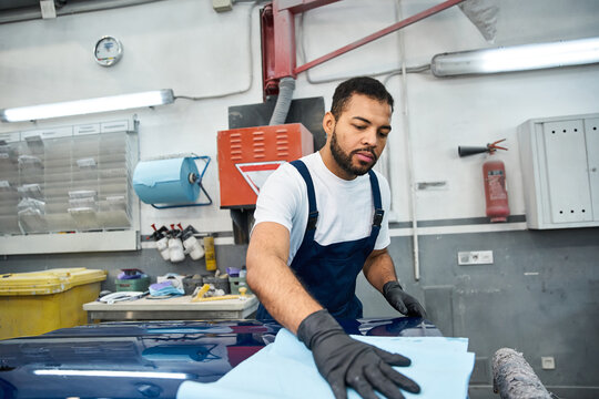 Passionate young mechanic works hard to restore a cars shine in a busy workshop environment.