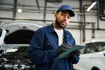 Skilled mechanic in uniform reviews notes with focus in a well lit automotive workshop setting