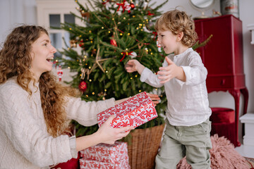 Family celebration with joyful child receiving Christmas gift near decorated tree during festive season