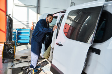 Young mechanic inspects a van while sunlight streams through the workshop windows