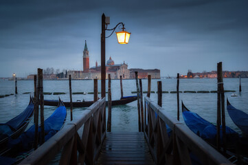 Evening view of gondolas at a pier with Venetian architecture illuminated by a street lamp