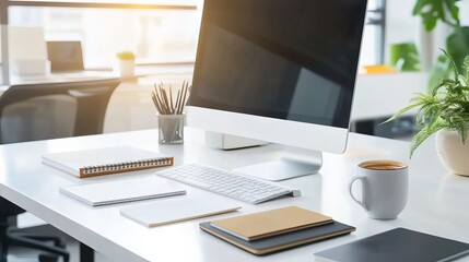 A close-up of an office desk with papers, a coffee mug, and a computer monitor displaying design software in the background. Bright daylight illuminates the scene, conveying a busy work environment. 