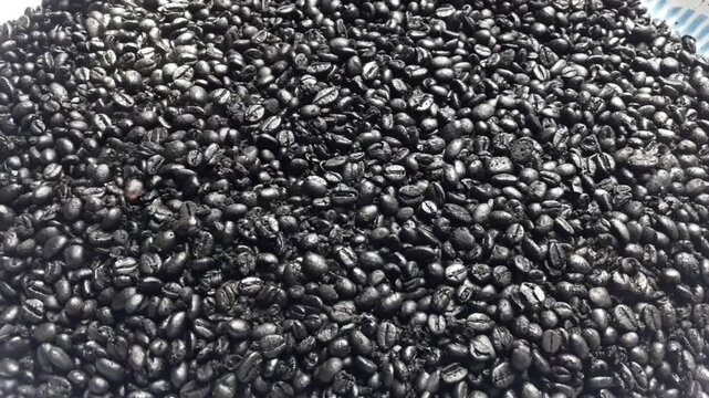 Piles of coffee beans in a pan with a puff of smoke on it. New black coffee beans are ready to be roasted and have a strong scented.