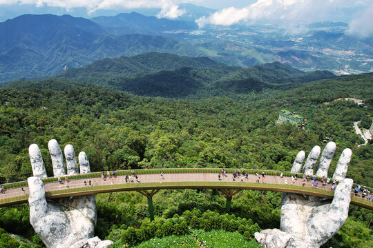 A statue depicting hands supporting a bridge over a lush forest Vietnam Da Nang Ba Na Hills Asia