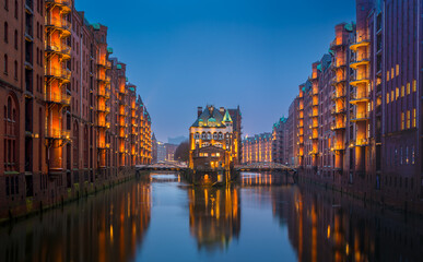 Illuminated canals reflect historic architecture at twilight in Hamburg