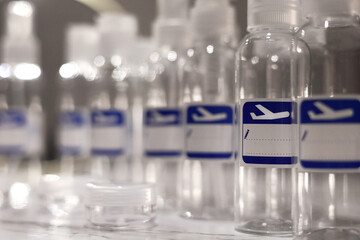 Small, transparent, plastic liquid bottles for plane traveling. Blank label with blue plane icon.