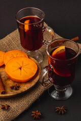 Delicious mulled wine with spices and sweet persimmons on a wooden plate