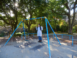 冬の公園で楽しくブランコを遊んでいる小学生の女の子の姿と銀杏の木の風景