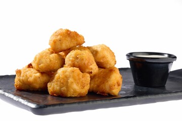 Close-up of crispy golden chicken nuggets piled on a black plate against a white background.
