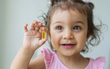 A cute little girl holding a vitamin d, or e, a, b or omega 3, fish, cod oil yellow capsule. Food supplement tablets for healthy life, medicine, and wellness.