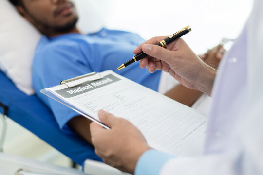 Doctor taking notes while patient explaining symptoms in hospital room. Doctor listens to a patient's symptoms in a hospital room, taking notes on a clipboard.