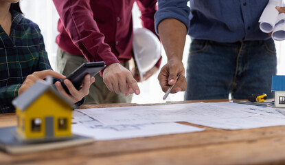Architects gather around table with house model and blueprints, discussing new project. Engaged in planning, teamwork in construction.