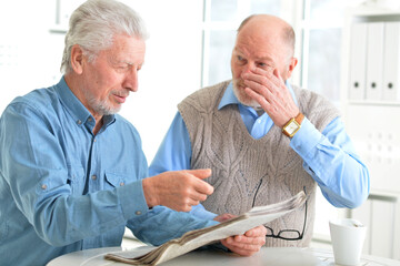 Two elderly men drinking coffee and reading newspaper