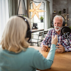 senior man host interviewer woman guest questions while record podcast