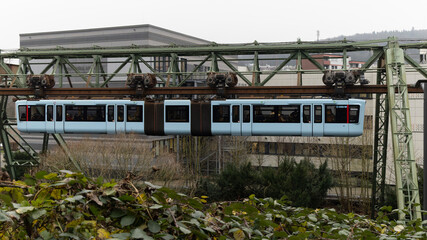 Ein blauer Schwebebahnwagen f&auml;hrt &uuml;ber der Wupper vorbei