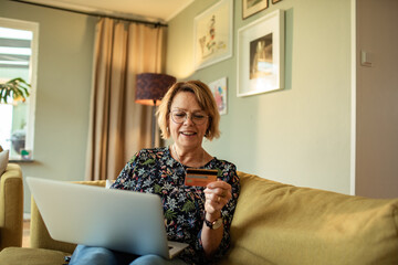 Smiling senior woman online shopping with credit card and laptop at home
