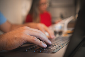 A man is typing on a laptop in front of a woman in a red shirt