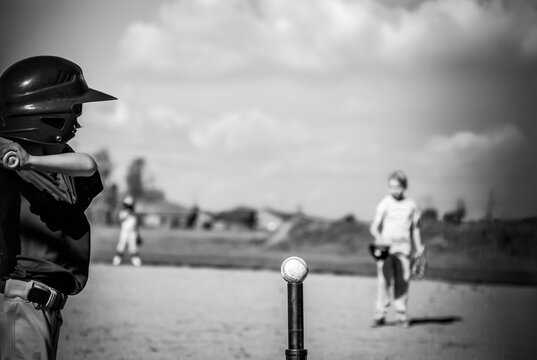 Youth batter hitting a tee ball into an open field at game