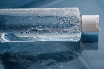 Bottle with cosmetic gel for face and body on blue background in water.